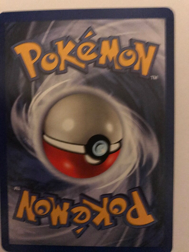 Puede incluir: Primer plano de una carta de intercambio de Pokemon con un borde azul y un fondo gris en espiral. El logotipo de Pokemon est&aacute; en la esquina superior derecha y el logotipo de Pokeball est&aacute; en la esquina inferior izquierda. La carta presenta una Pokeball con un dise&ntilde;o rojo y blanco.