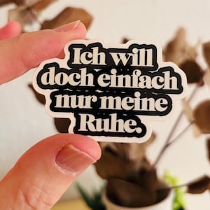 Könnte beinhalten: Ein gestanzter Aufkleber mit dem deutschen Text Ich will doch einfach nur meine Ruhe in einer fetten, schwarzen, retro-inspirierten Schriftart mit weißer Umrandung. Der Aufkleber hat eine wellenförmige, organische Form, die den Buchstaben folgt.