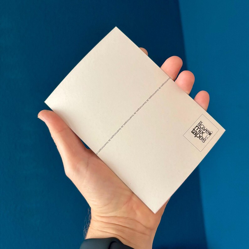 May include: A rectangular, off-white card held in a hand, with the words "ilove mixtapes" in a square logo on the lower right. The card has text along the top edge. The background is a solid, deep blue.