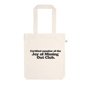 Könnte beinhalten: Eine cremefarbene Stofftasche aus Segeltuch mit zwei Schulterriemen und einem kleinen grünen Etikett an der Seite. Auf der Vorderseite steht in schwarzer Schrift: Certified member of the Joy of Missing Out Club. Die Tasche ist rechteckig.