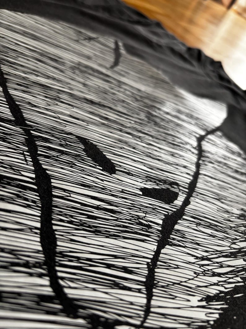 May include: Abstract black and white artwork. The design features a series of thin, horizontal lines with thick, black, vertical strokes and splatters. The artwork is on a white background, with a black fabric draped over it.