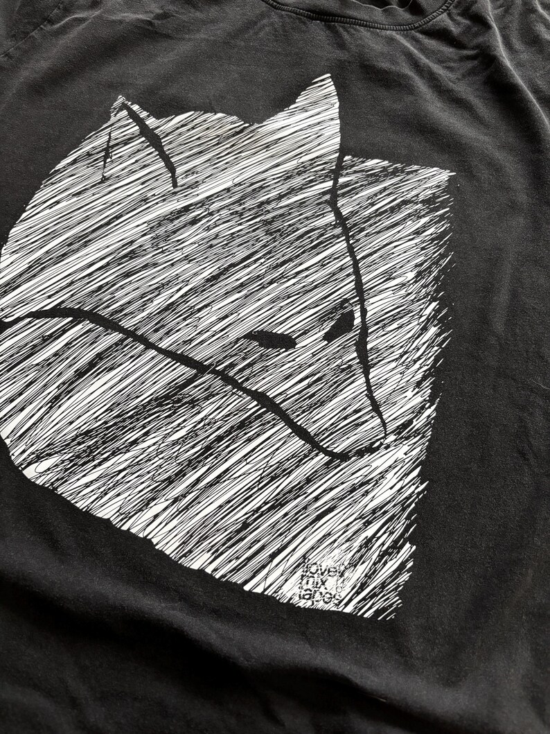 May include: Black t-shirt featuring a white, stylized illustration of a fox's head. The design uses a cross-hatching technique to create texture and depth. The text "love mix tapes" is printed at the bottom.