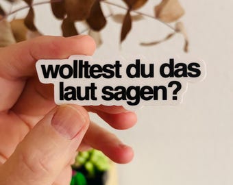 May include: A white die-cut sticker with a black sans-serif font featuring the German text "wolltest du das laut sagen?". The sticker has a clean, rounded border and is presented against a neutral background, highlighting the bold, legible lettering.