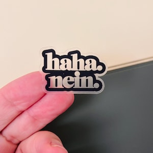 Könnte beinhalten: Ein gestanzter Aufkleber mit dem Text "haha. nein." in einer fetten, abgerundeten, schwarzen serifenlosen Schrift. Die Buchstaben haben eine metallisch silberne Oberfläche, die Licht reflektiert, und der Aufkleber hat einen transparenten Rand.