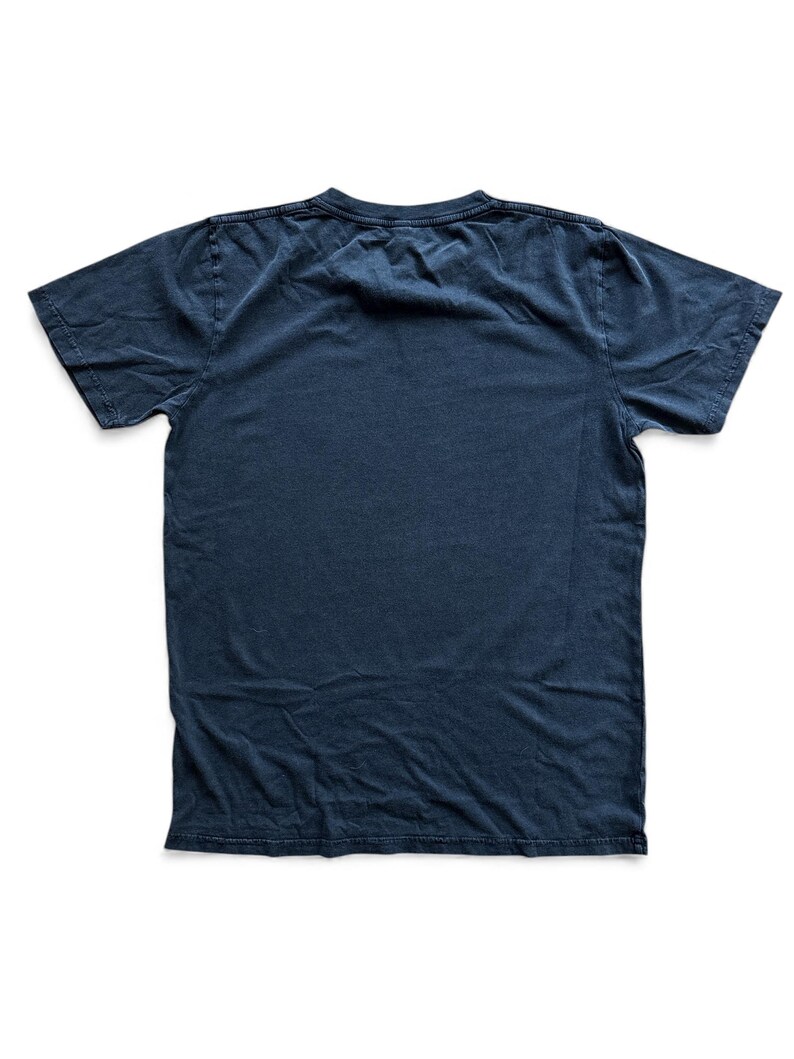 May include: A navy blue, short-sleeved t-shirt, laid flat on a white surface. The shirt has a crew neck and appears to be made of a soft, worn material. The fabric has a slightly faded appearance, suggesting it has been washed.