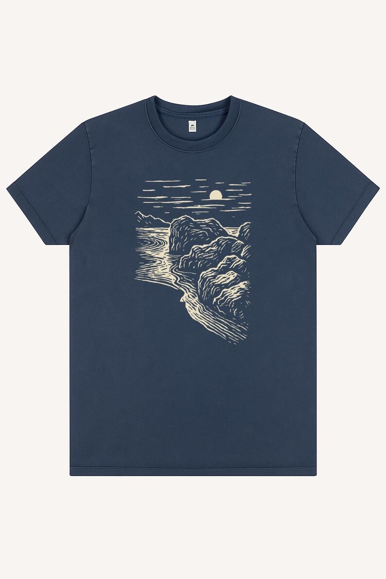 Pu&ograve; includere: T-shirt blu navy con un disegno di paesaggio color crema. La grafica raffigura una costa con rocce, acqua e un sole o una luna. La maglietta ha un girocollo e maniche corte.