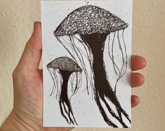 May include: A black and white art print featuring two jellyfish illustrations. The jellyfish are drawn with intricate line work, creating a textured appearance. The print is held in a hand, showcasing the size and detail of the artwork.