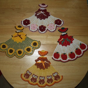 May include: Four crocheted doilies featuring different designs. The doilies are shaped like a circle with a scalloped edge. The designs include a sunflower, an owl, an apple, and a flower.