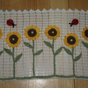 Pode incluir: Um corredor de mesa branco de crochê com um design de girassóis e joaninhas. O corredor apresenta cinco girassóis amarelos com centros marrons e caules e folhas verdes. Duas joaninhas vermelhas estão posicionadas acima dos girassóis.