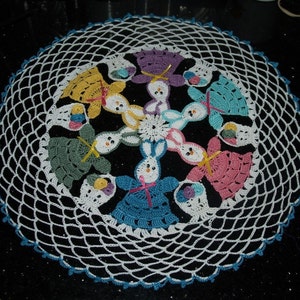 May include: A white crocheted doily with a blue border features eight crocheted bunnies in various colors, including pink, green, yellow, and blue. Each bunny holds a basket of colorful eggs.
