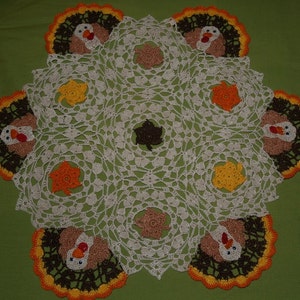 May include: A white crocheted table runner with a Thanksgiving theme. It features seven brown turkeys with orange and yellow feathers, and brown leaves.