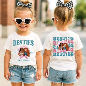 A young girl wearing a white t-shirt with a graphic design and text, smiling and wearing sunglasses.