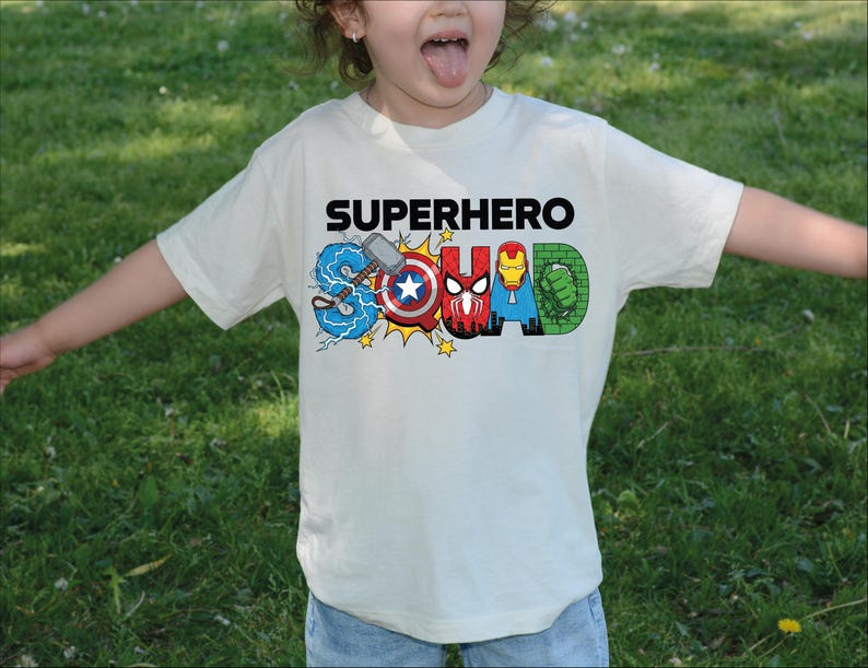 A young child wearing a white t-shirt with the text "SUPERHERO" printed on it, surrounded by various superhero logos and characters.