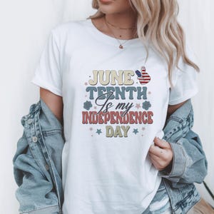 May include: White t-shirt with the text "June Tenth Is my Independence Day" in a retro font. The design includes stars and a peace sign with a red, white, and blue color scheme. The shirt is worn with a denim jacket.