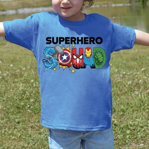 A child wearing a blue t-shirt with the text "SUPERHERO SQUAD" printed on it, featuring various superhero characters.