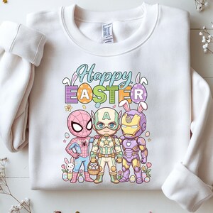 A white sweatshirt with a colorful graphic design featuring three cartoon characters - Spider-Man, Captain America, and Iron Man - along with Easter-themed elements such as eggs and flowers.