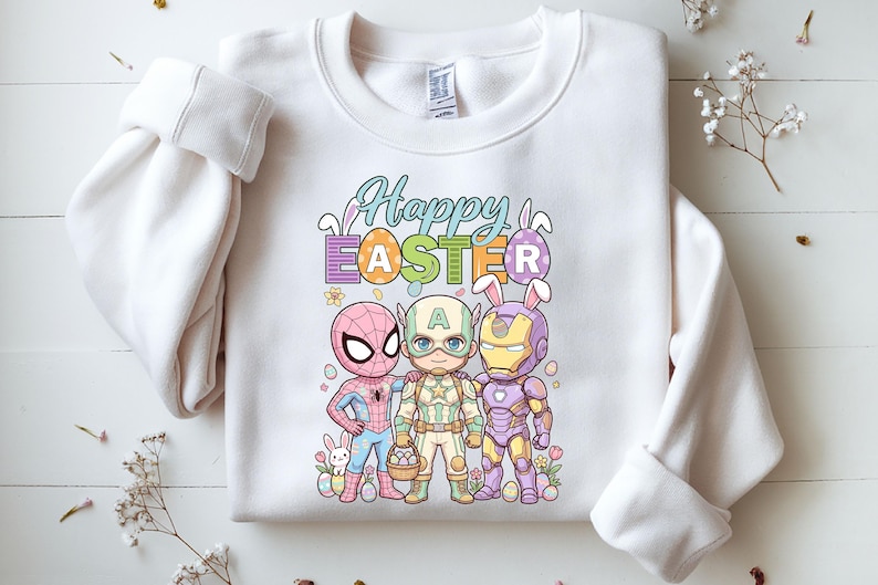 A white sweatshirt with a colorful graphic design featuring three cartoon characters - Spider-Man, Captain America, and Iron Man - along with Easter-themed elements such as eggs and flowers.