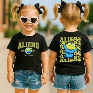 A young girl wearing a black t-shirt with a cartoon character and the text "Aliens" on it, along with a heart-shaped pair of sunglasses.