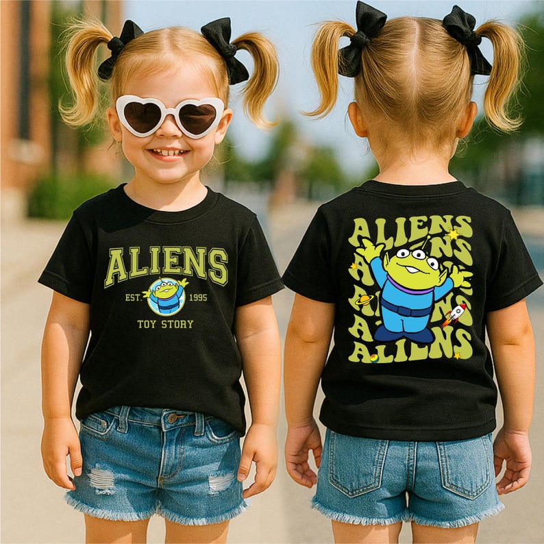 A young girl wearing a black t-shirt with a cartoon character and the text "Aliens" on it, along with a heart-shaped pair of sunglasses.