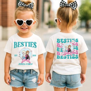 A young girl wearing a white t-shirt with a graphic design and text, smiling and wearing a bow in her hair.