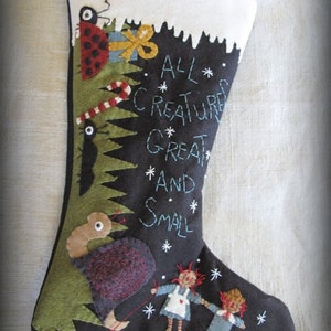 May include: A black felt Christmas stocking with a green felt tree, a red ladybug, a candy cane, and the text "ALL*CREATURES*GREAT*AND*SMALL". The stocking also features a brown felt turkey, two rag dolls, and white snowflakes.