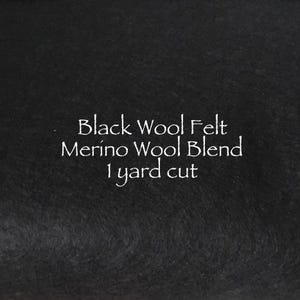 May include: Black wool felt, merino wool blend, 1 yard cut. The image shows a close-up of a black felt fabric with white text. The text indicates the material is a merino wool blend, sold by the yard.