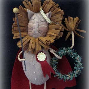 Peut inclure: Une décoration de lion en feutre faite à la main avec une cape rouge, une couronne dorée et une couronne de verdure. Le lion tient un bâton avec une boule dorée au sommet.