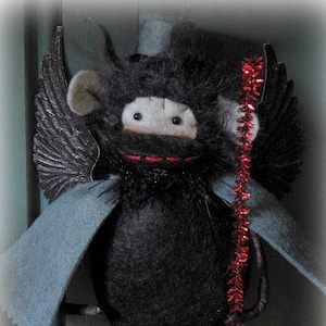 Puede incluir: Un juguete de peluche negro y blanco con un sombrero de copa, alas y una serpentina rizada roja y blanca. El juguete tiene un cuerpo de peluche negro y una cara blanca con ojos negros.