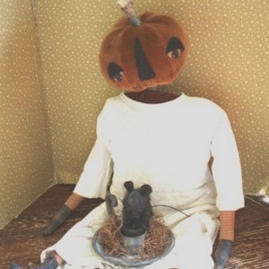 Peut inclure: Une poupée de chiffon faite à la main avec une tête de citrouille et une robe blanche. La poupée est assise sur un sol en bois avec une petite souris noire et un bougeoir en métal.