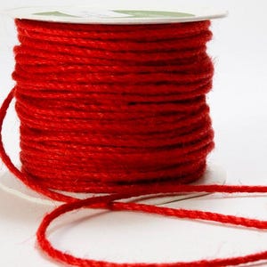 May include: A spool of bright red twine. The twine is tightly wound around a white cardboard core. A length of the twine extends from the spool, suggesting it is ready for use. The twine has a slightly textured appearance.