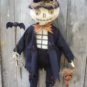 May include: A handmade Halloween decoration of a skeleton wearing a black top hat, suit jacket, and pants. The skeleton is holding a stick with a bat on top.