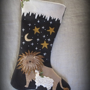 May include: A black felt Christmas stocking with a white felt cuff and a snowy scene. The stocking features a lion and a lamb with a holly sprig, and a night sky with stars and a crescent moon.