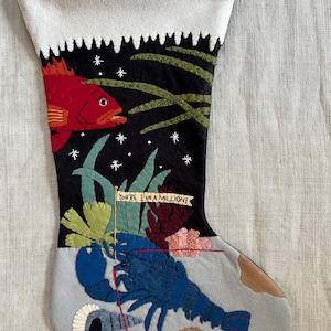 May include: A Christmas stocking with an underwater theme. The stocking features a red fish, a blue lobster, and the text "You're 1 in a million!" against a black background with white stars and green seaweed.