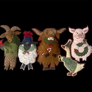 May include: Five felt Christmas ornaments depicting a goat, sheep, cow, pig, and goose. Each ornament is wearing a festive green and red outfit and holding a holiday-themed item.