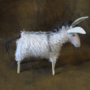 May include: A gray and white plush donkey with black yarn for a tail and mane. The donkey has a long, floppy ear and a white, felt nose.