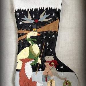 May include: A felt Christmas stocking with a black background and white snowflakes. The stocking features a white goose wearing a top hat and green scarf, a red fox, a gray cat wearing a red scarf, and two blue birds with a red heart.