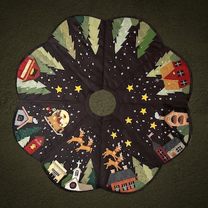 May include: A black felt Christmas tree skirt with a whimsical winter scene. The skirt features embroidered details of houses, trees, stars, and reindeer. The text "Post Office" and "School" are also embroidered on the skirt.
