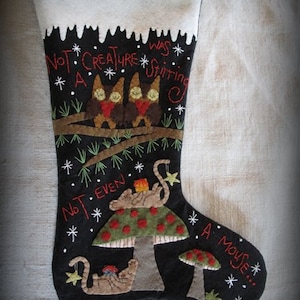 May include: A black felt Christmas stocking with a white cuff. The stocking is decorated with a winter scene featuring three brown creatures sitting on a branch, a cat sleeping on a mushroom, and the text "Not a creature was stirring, not even a mouse..."