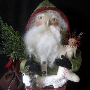 May include: A handmade felt Santa Claus doll wearing a green and red hat and holding a felt doll in a stocking. The Santa doll is standing in a brick chimney.
