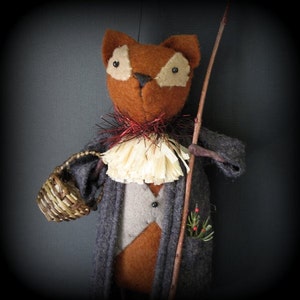 Könnte beinhalten: Eine handgefertigte Filz-Fuchs-Puppe, die einen grauen Mantel, einen rot-weißen Kragen trägt und einen Stock hält. Der Fuchs trägt einen kleinen geflochtenen Korb und hat einen Zweig Grün mit roten Beeren in seiner Tasche.