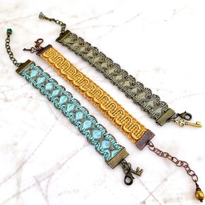 Puede incluir: Tres pulseras con dise&ntilde;os intrincados y cierres en forma de llave. Las pulseras est&aacute;n hechas de tejido tejido y cuentas en tonos de azul, dorado y verde.