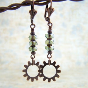 May include: A pair of copper-toned earrings with green glass beads and a gear design. The earrings have a clip-on closure.