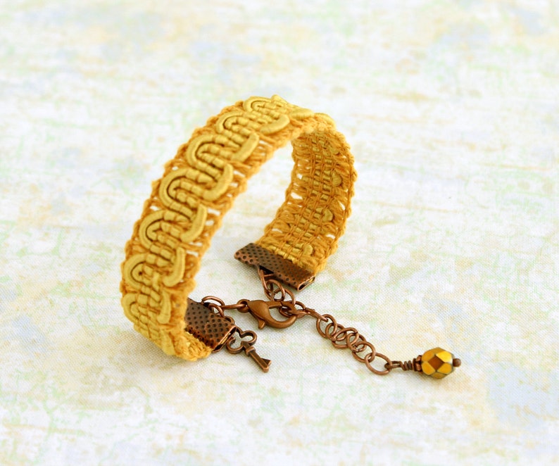 Puede incluir: Un brazalete de crochet amarillo con un cierre de lat&oacute;n y un peque&ntilde;o abalorio de cuentas doradas.