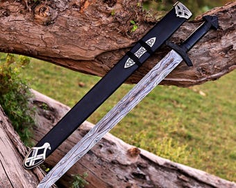 May include: A sword with a patterned Damascus steel blade and a black hilt, accompanied by a matching black scabbard. The scabbard features silver-toned metal accents with intricate knotwork designs at the tip and near the throat.