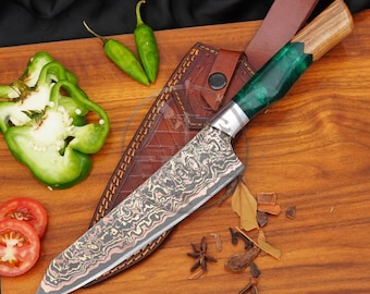 May include: A chef knife with a patterned Damascus steel blade, a green resin and wood handle, and a brown leather sheath. The knife is displayed with two green chili peppers, two tomato slices, and star anise on a wooden surface.