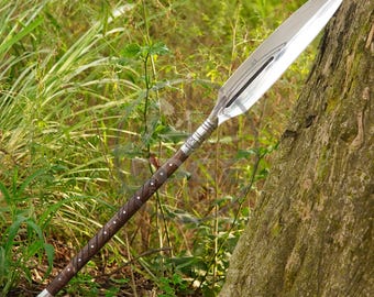May include: A spear featuring a long, pointed, double-edged silver metal blade with a central ridge. The shaft is made of dark brown wood, wrapped with a diagonal pattern of thin metal wire, and finished with a silver metal cap at the base.