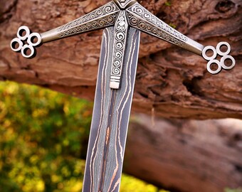 May include: A sword featuring a dark, layered Damascus steel blade with visible wavy patterns. The metal crossguard displays intricate scrollwork, a central lion emblem, and four-ringed terminals at each end of the quillons.