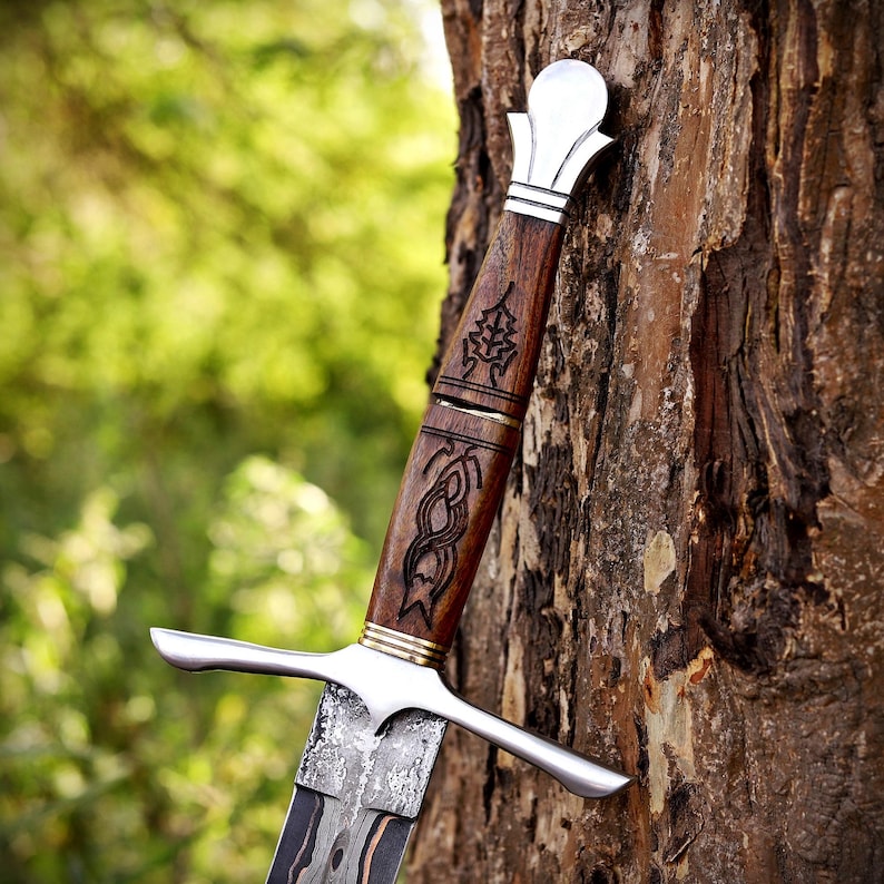 May include: A dagger with a dark wood handle featuring intricate black etched patterns, a polished silver-toned pommel, a matching silver-toned crossguard, and a patterned metal blade with a dark, textured finish along the central section.