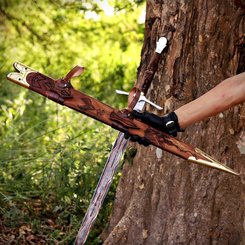 May include: A sword with a patterned metal blade and a wooden hilt, accompanied by a wooden scabbard featuring intricate carvings, brass-colored metal accents at the ends, and brown leather straps for securing the weapon in its sheath.