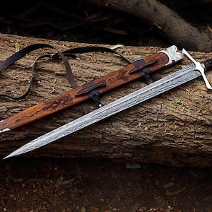 May include: A double-edged sword with a patterned Damascus steel blade, a silver crossguard, and a dark wooden handle with a silver pommel. It is accompanied by a matching wooden scabbard featuring intricate carvings and a black leather strap.